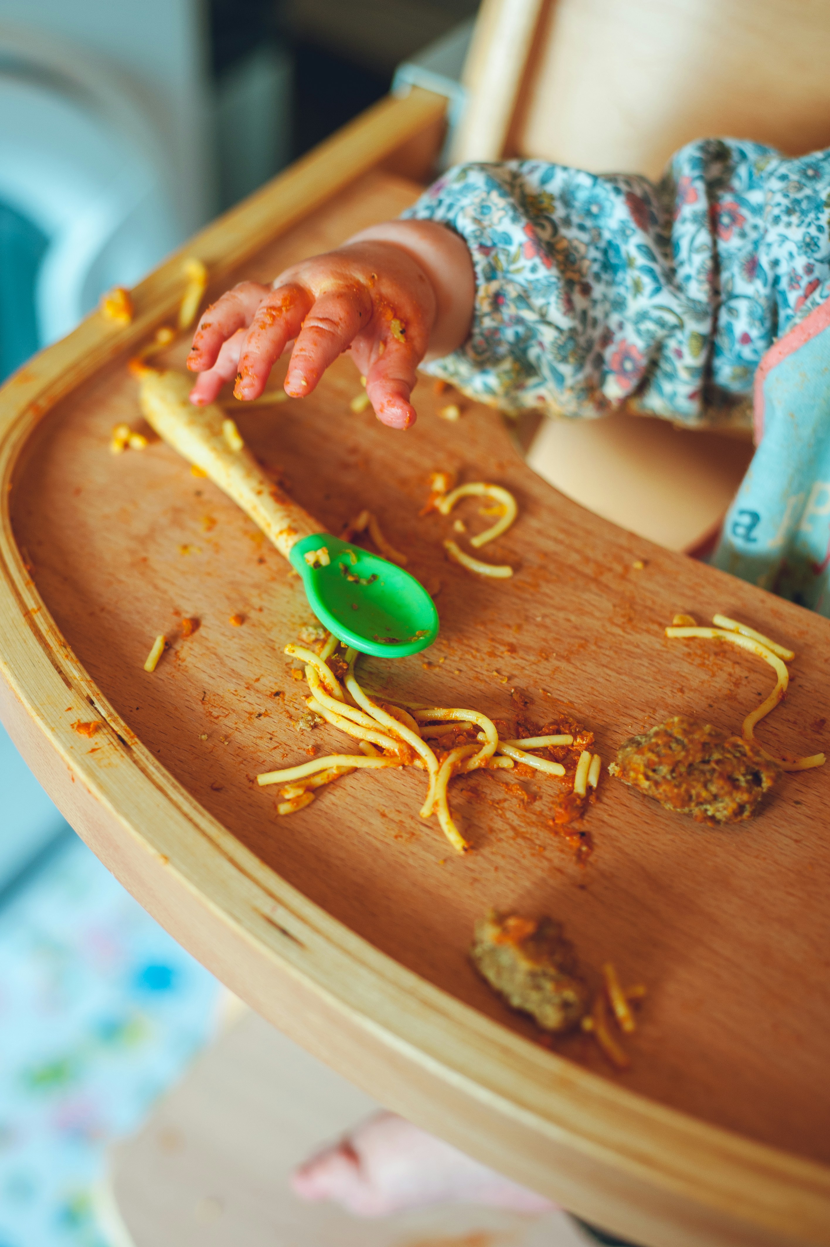 mani di un bambino sul seggiolone che mangia spaghetti